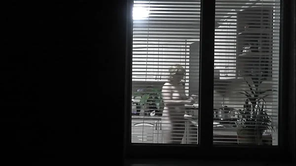 Peeping. Voyeur. Neighbor pervert voyeur in evening on street looks out window as naked sexy neighbor in kitchen prepares dinner for her husband. Naked in public. Naked at home. Family.  Outdoor